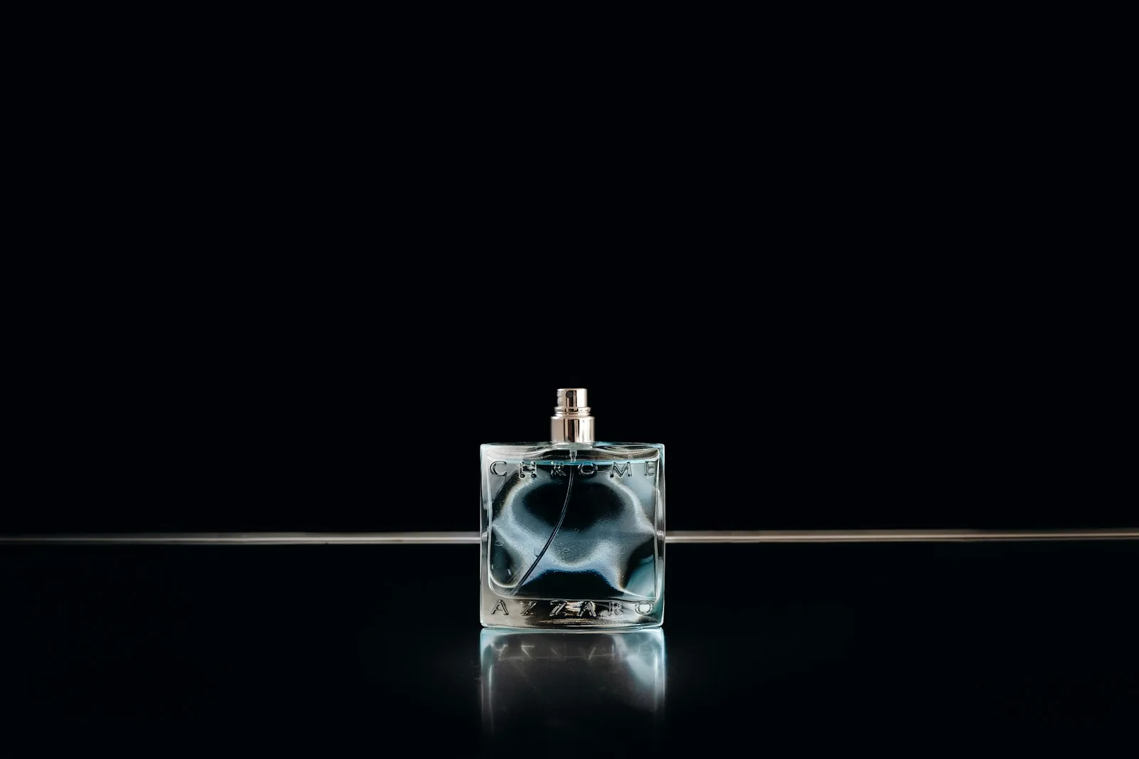 Flacon de parfum en verre sur fond noir, reflets argentés