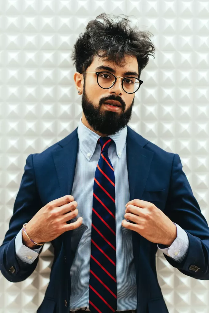 Homme barbu en costume bleu marine, chemise bleu ciel et cravate rayée