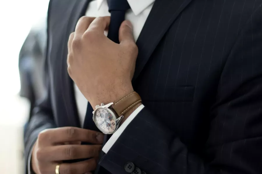 Homme en costume noir qui ajuste sa montre au poignet