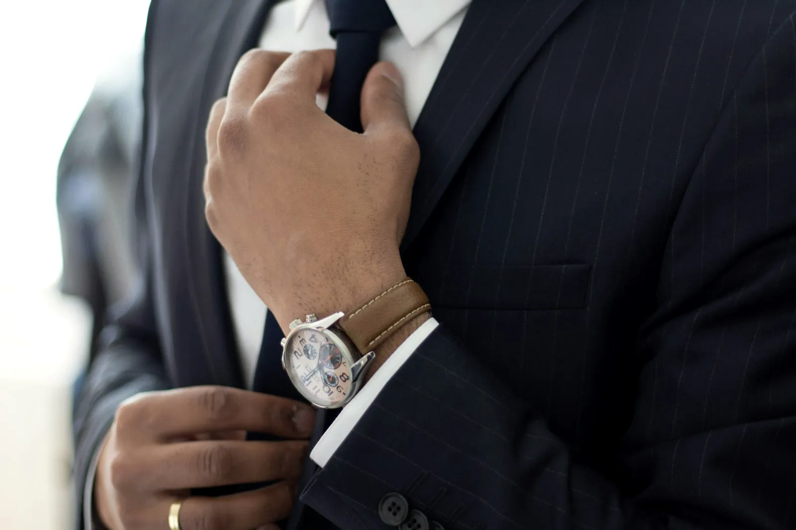 Homme en costume noir qui ajuste sa montre au poignet