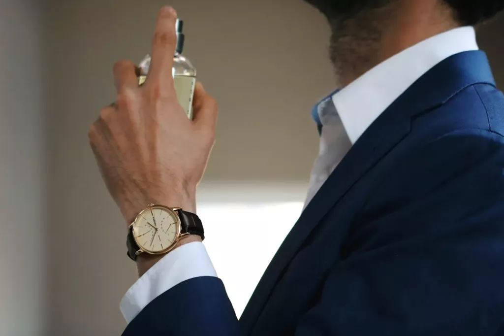 Homme en costume bleu qui vaporise son parfum, montre au poignet