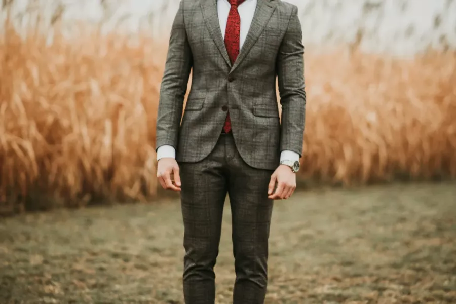 Homme en costume gris et cravate rouge dans un champ d’herbes hautes