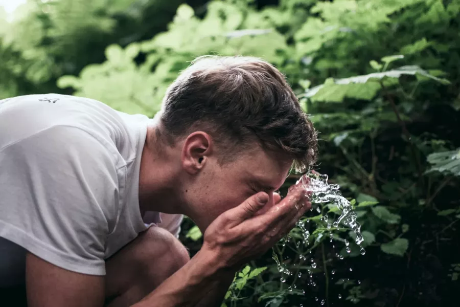 Homme qui se rince le visage à l’eau fraîche en plein air