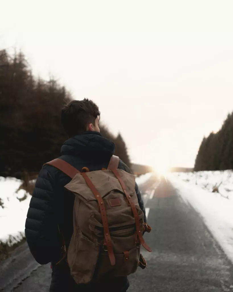 Voyageur avec un sac à dos en cuir sur une route enneigée